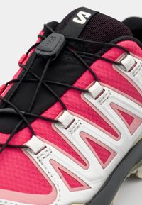 Red and pink trail shoe featuring a textured upper, black lacing system, and white accents with triangular cutouts on the side.