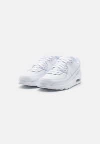 Chaussures de sport blanches avec un dessus en cuir lisse et en mesh, design à lacets, col rembourré et coussin d'air visible dans la semelle.