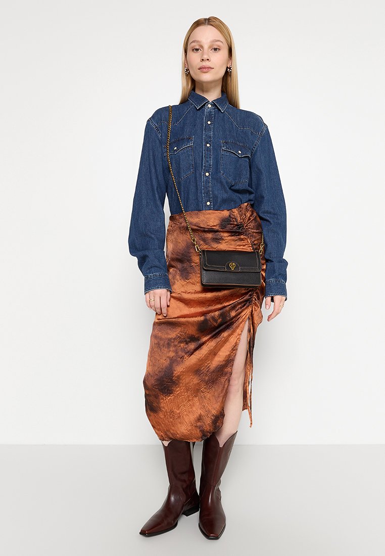 Chemise en denim avec col, deux poches poitrine et fermeture à boutons, associée à une jupe asymétrique marron tie-dye. Bottes marron jusqu'aux genoux.