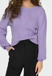 Pull en maille côtelée lilas avec un col rond, un motif en losanges et des manches légèrement bouffantes, associé à un pantalon noir.