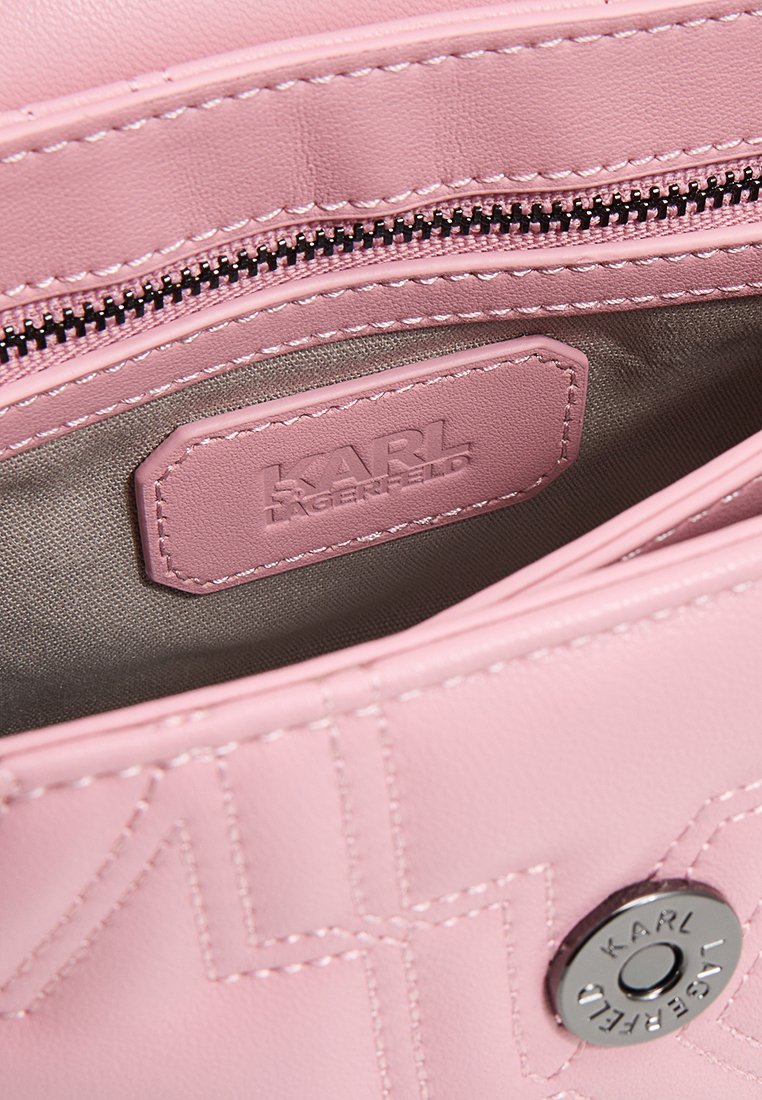 Intérieur d'un sac à main en cuir rose montrant une poche zippée, une étiquette en relief KARL LAGERFELD, et un bouton-pression argenté avec le nom de la marque gravé.