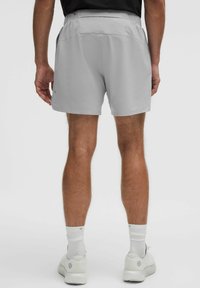 Pantalones cortos deportivos de color gris claro con un corte relajado, cinturilla elástica y bolsillos. Llevados con zapatillas deportivas blancas y calcetines claros.