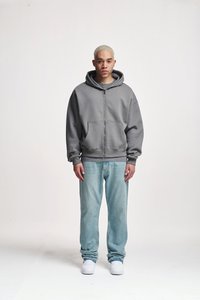 Grauer Zip-Hoodie mit großer Fronttasche und gerippten Bündchen, kombiniert mit hellblauen Jeans und weißen Sneakern. Einfaches, lässiges Design.
