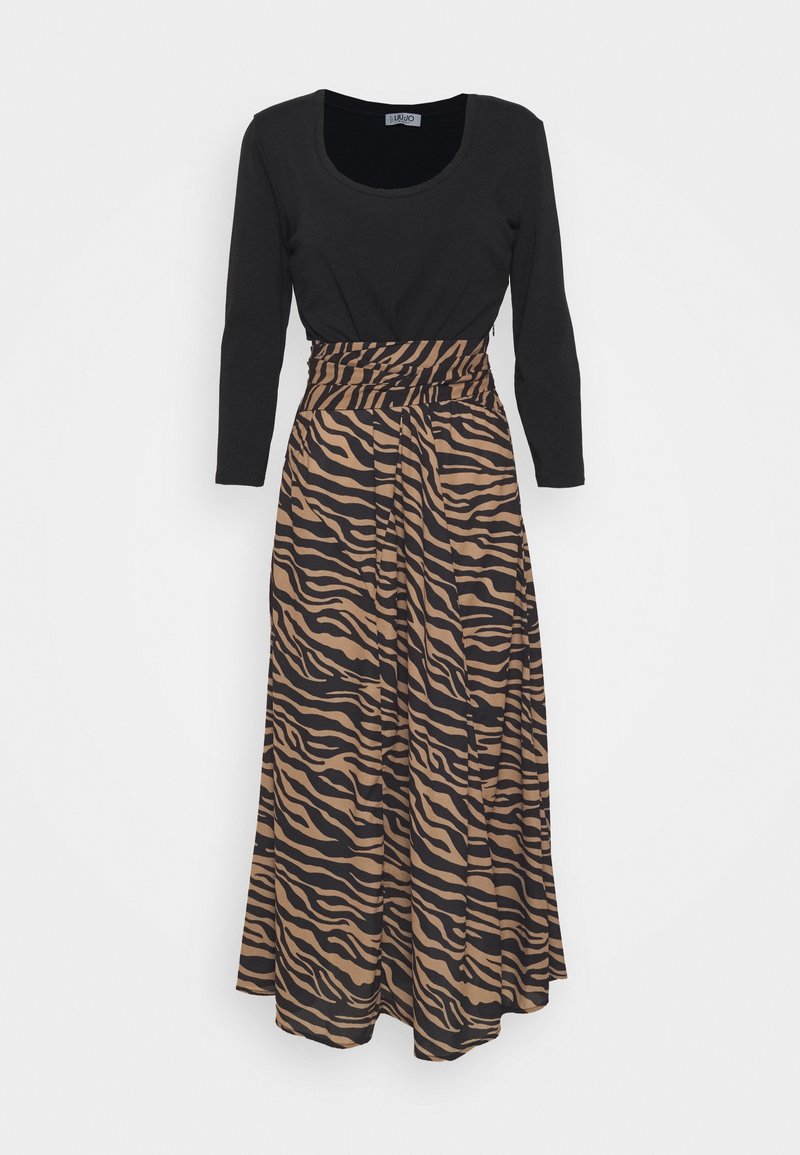 Haut noir à manches longues associé à une jupe midi taille haute rayée zèbre marron et noir avec une ceinture froncée.