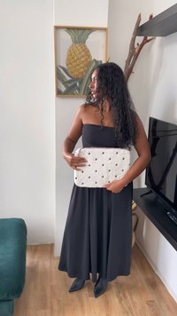White fuzzy bag with black floral embroidery, rectangular shape, zip closure, held by a person in a black strapless dress against a neutral background.