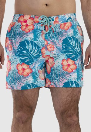 Man wearing blue swim shorts with pink and orange hibiscus flowers and large tropical leaves, front view showing waist to mid-thigh.