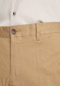 Beiga linbyxor med en slät textur, som har knappstängning och sydda detaljer vid midjan och sid sömmen.