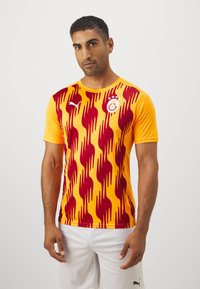 Maglietta sportiva da uomo di colore giallo con motivi a fiamma rossa. Presenta un collo rotondo, maniche corte e accenti del logo sul petto.