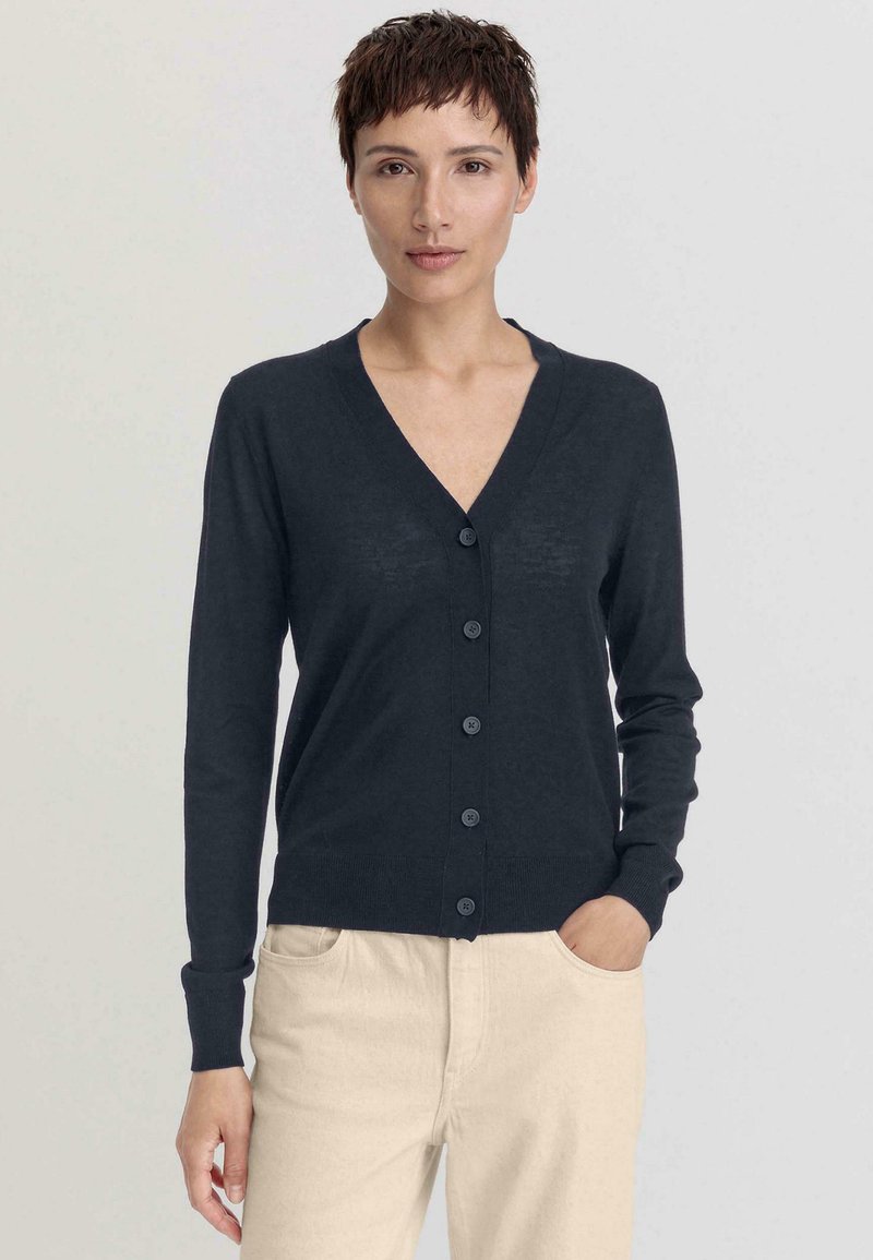 Cardigan marine foncé avec un col en V, des manches longues et six boutons assortis sur le devant. Tissu tricoté doux et léger avec des poignets côtelés.