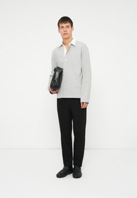 Hallid pika varrukaga hall polo särk valge kraega, kombineeritud mustade pükstega ja mustade jalatsitega, hoides musta käekotti. Minimalistlik disain.