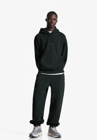 Čierna mikina s predným vreckom a sťahovacou šnúrkou; zodpovedajúce čierne tepláky s manžetovými lemami; spárované so šedými a bielymi teniskami.