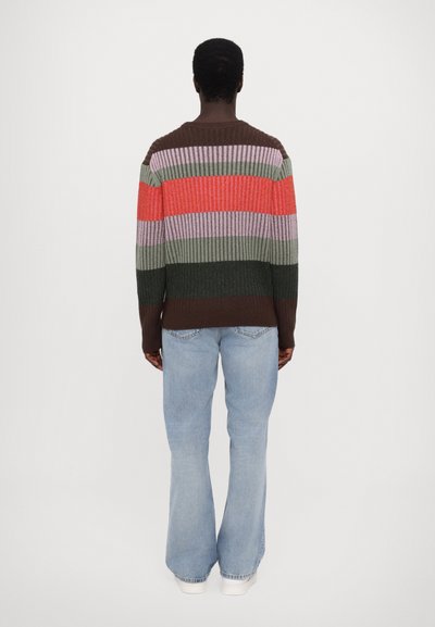 Multicolored striped sweater with ribbed texture in red, pink, green, and brown; paired with light blue flared jeans.