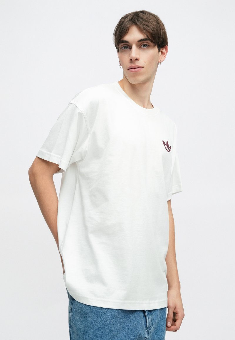 Witte katoenen t-shirt met een ronde hals en korte mouwen, met een bordeauxrode Adidas-logo op de linkerborst. Gemaakt in combinatie met denim jeans.