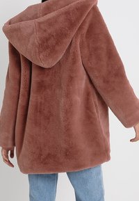 Chaqueta con capucha de piel sintética en un suave color malva, con un ajuste holgado, mangas largas y una superficie texturizada para ofrecer calidez y comodidad.