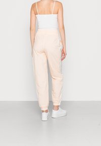 Světle broskvové tepláky s elastickým páskem a manžetami. Mají bílé boční panely a hladkou, textura látku s uvolněným střihem.