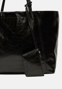 Czarna skórzana torba na ramię o błyszczącej powierzchni, z zamykanym portfelem przymocowanym na pasku. Subtelne oznaczenia marki na obu przedmiotach.