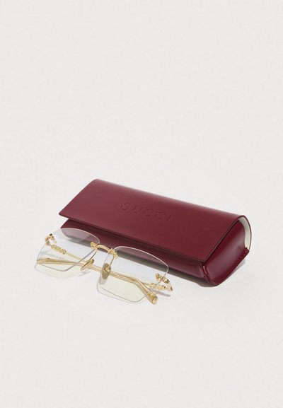Gucci piros bőr szemüvegtok dombornyomott logóval, mellékelve átlátszó szemüveggel arany színű szerkezeti elemekkel és díszített oldalsó díszítésekkel.