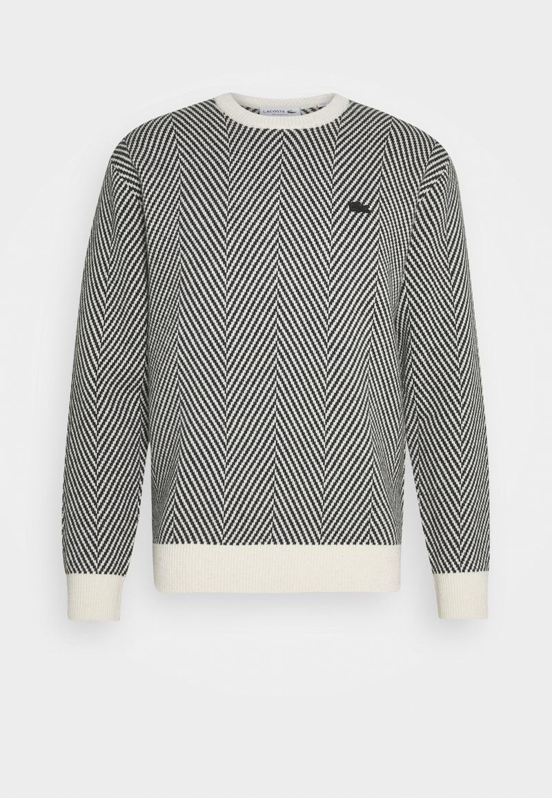 Svart och vit herringbone-mönstrad crewneck-tröja med vita muddar och nederkant, med en liten svart broderad logotyp på bröstet.