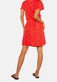 Robe rouge à fleurs avec manches courtes et jupe évasée, motifs de fleurs blanches, en tissu léger et doux.