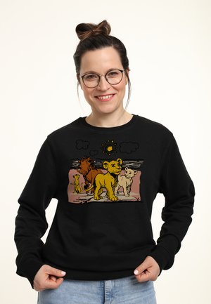 Sudadera negra con un estampado gráfico de cachorros de león y un sol. El diseño incluye amarillos brillantes, marrones y colores claros con un fondo texturizado.
