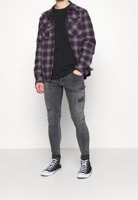Camisa de franela a cuadros en negro, gris y burdeos; camiseta negra; jeans skinny desgastados en gris; zapatillas altas negras.