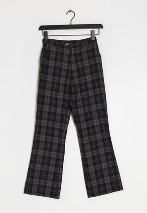 Pantalones con estampado de cuadros en negro y gris con líneas rojas sutiles, colgados en una percha negra sobre un fondo blanco.