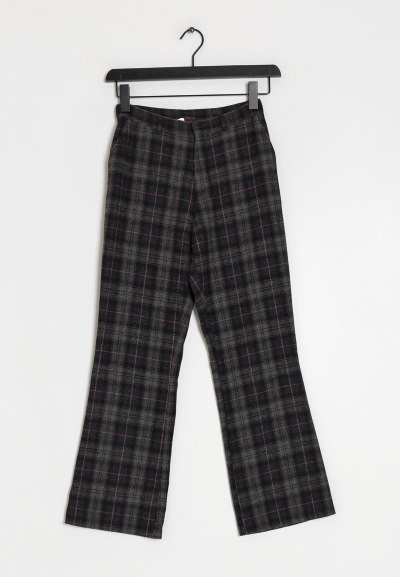 Pantalon à carreaux noirs et gris avec des fines lignes rouges, suspendu sur un cintre noir sur fond blanc.