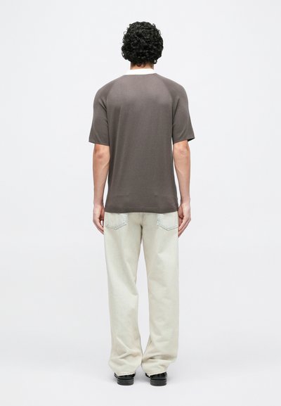 Chemise marron à manches courtes raglan, texture douce, encolure ronde, associée à un pantalon large de couleur claire.