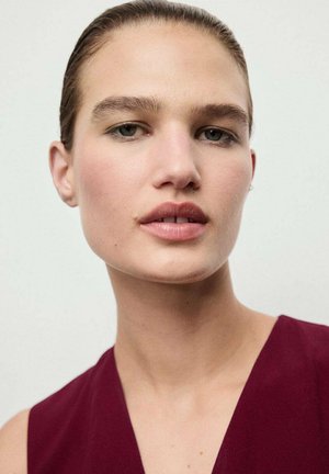 Close-up van een gezicht met een gladde huid. Het onderwerp heeft lichtbruin haar en draagt een diep bordeauxkleurig topje. Zachte make-up benadrukt de natuurlijke kenmerken.