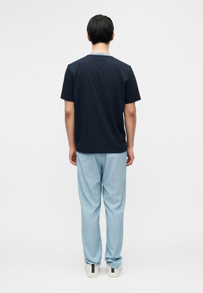 Μπλε ναυτικού χρώματος κοντομάνικη μπλούζα με κλασική εφαρμογή, συνδυασμένη με ανοιχτό μπλε παντελόνι με ρίγες και λευκά αθλητικά παπούτσια με μεταλλικές λεπτομέρειες.