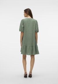 Zelena haljina nabrana s kratkim puf rukavima, napravljena od teksturirane tkanine. Ima okrugli izrez i pada iznad koljena.