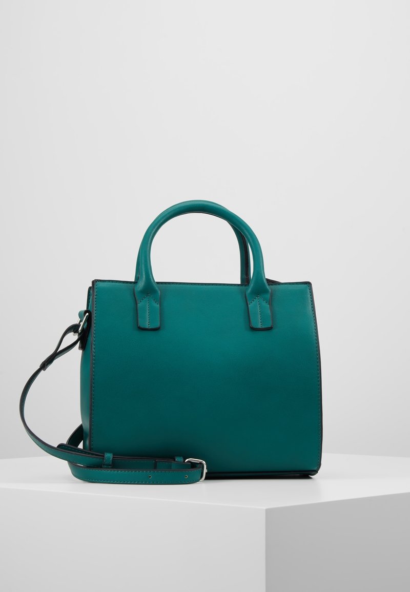 Sac à main en cuir bleu sarcelle avec deux poignées supérieures et une bandoulière amovible, exposé sur un socle blanc sur fond uni.