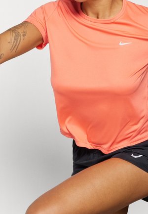 Nike T-shirt met korte mouwen in koraal, met een ronde halslijn en een zachte textuur, gecombineerd met zwarte shorts met een subtiel logo-detail.