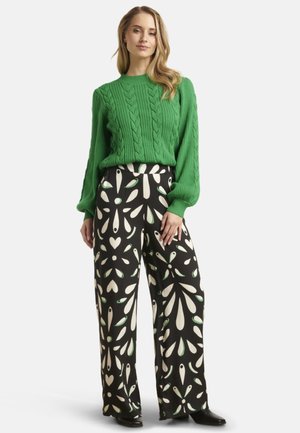 Green cable-knit sweater with a round neckline paired with high-waisted black wide-leg pants featuring a white and green leaf pattern.