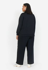 Sudadera negra y pantalones de pierna ancha hechos de tela suave. El conjunto cuenta con mangas largas y un corte relajado, y tiene un diseño y acabado sencillos.