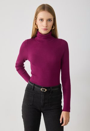 Tettskjorte med høy hals i ribbet tekstur, livlig magenta farge, paret med høy midje sorte jeans og et enkelt svart belte.
