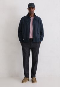 Granatowa kurtka bomberka, jasnoróżowy T-shirt, ciemne spodnie we wzory oraz beżowe buty. Czapka również jest granatowa, dopełniając casualowy strój.