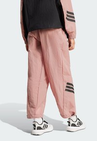 Light pink joggers with a crinkled texture, elastic waistband, and side pockets, paired with black and white athletic shoes featuring stripes.