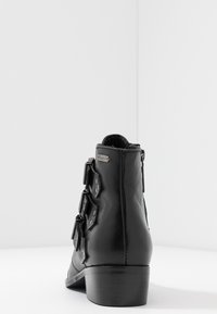 Černé kožené kotníkové boty s kulatou špičkou, zipovým zapínáním a dekorativními pásky. Zesílený důlek a hladká textura.