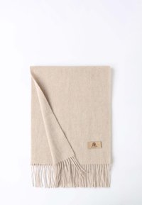 Sciarpa di lana beige chiaro con bordi frangiati e una piccola etichetta con logo. Il tessuto ha una consistenza morbida e una finitura liscia.