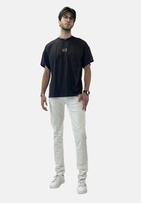 T-shirt nera di cotone con grafica di New York, abbinata a pantaloni di denim bianchi e sneakers bianche. Modello con occhiali e orologio al polso.