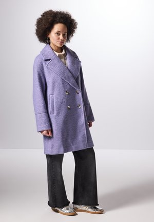 Lila dubbelzijdige jas met een gestructureerde afwerking, grote revers en voorzakken, gecombineerd met flared zwarte jeans en zilveren schoenen.