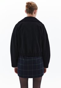 Czarna krótka kurtka z długimi rękawami i elastycznym dołem, w połączeniu z krótką spódnicą w kratę w ciemnoniebieskie i zielone wzory.