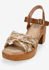 Brown leather strap sandal with a woven natural fiber upper accented with gold threads, featuring a chunky wooden heel and a buckle closure.