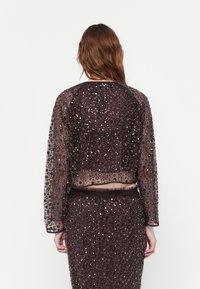 Bordeaux gekleurde cropped jasje met lange mouwen, transparante textuur en decoratieve pailletten. Beschikt over een bijpassende tailleband en een aansluitende pasvorm.