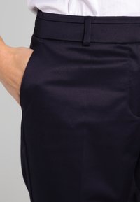 Námořnické kalhoty s hladkou texturou, s klasickým pasem a bočními kapsami, zobrazené od pasu po stehna.