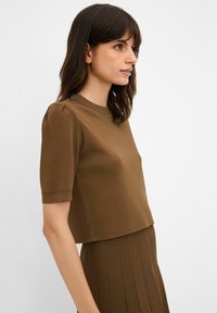Hnědý top s krátkým rukávem, mírně zkrácený, s žebrovanou texturou a šitými detaily na rukávech, který působí čistým, minimalistickým stylem.