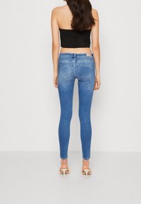 Jeans de denim azul ajustados con un ligero desgaste, que cuentan con un diseño de cinco bolsillos, cintura de altura media y un detalle de costura clásica.