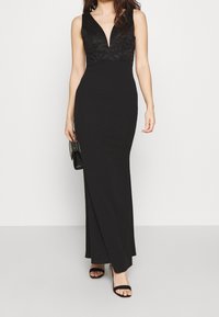 Svart aftonklänning med en djup urringad spetsöverdel och en figurnära kjol, med en slät textur och en golvslängd design.