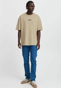 Beige oversized t-shirt with "Actions Decisions" printed in black, paired with light blue jeans and gray sneakers with white stripes.